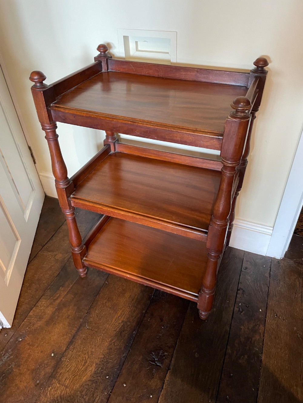 A three-tiered mahogany dumb waiter featuring turned support columns, corner finials, and raised galleries around the shelves.