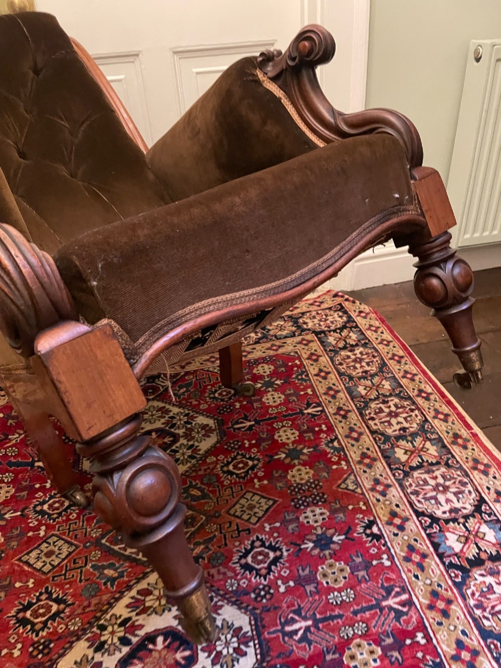 A Victorian mahogany library chair featuring dark brown velvet button-tufted upholstery, carved scroll arms, and brass castors. View IV