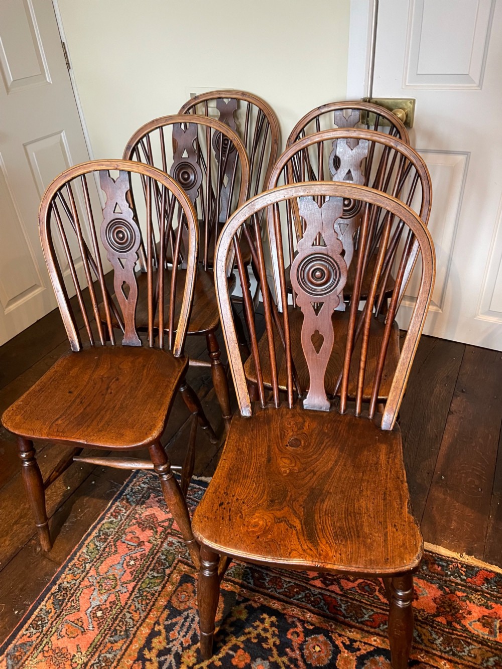 A set of six warm brown elm wheelback dining chairs featuring hoop backs, carved central splats, and turned legs.