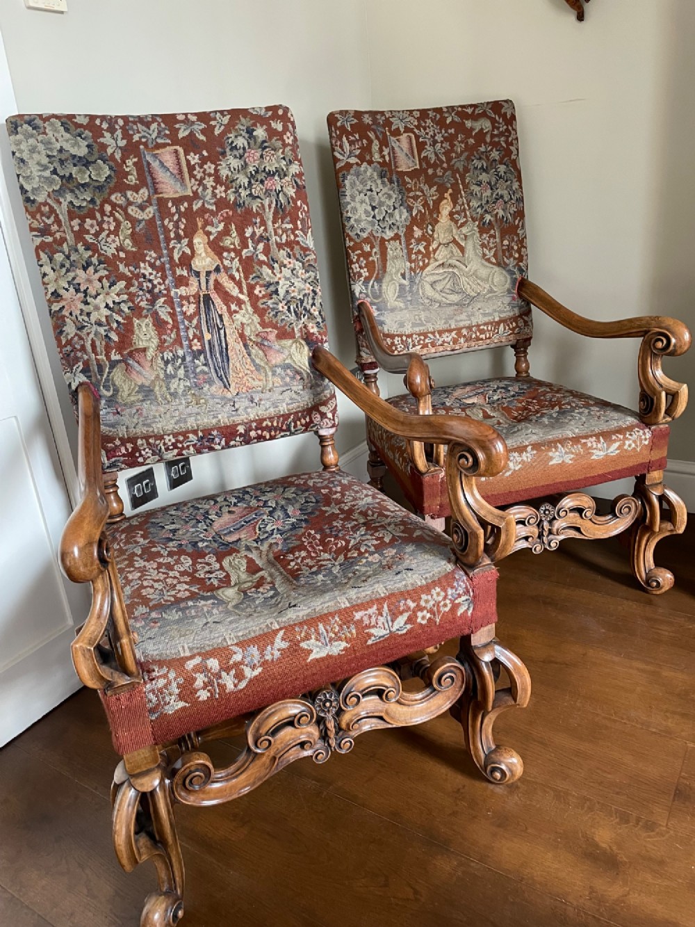 A pair of high-backed William and Mary style walnut armchairs with scroll arms, carved decorative stretchers, and pictorial woven tapestry upholstery. View II