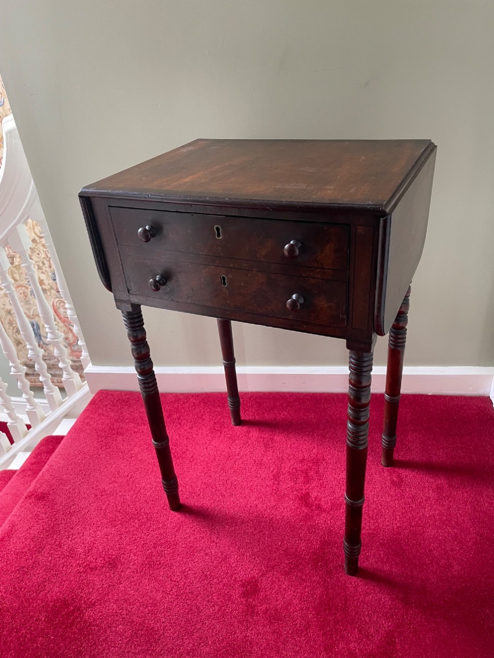 A dark mahogany drop-leaf side table featuring two drawers with wooden knobs and four slender turned legs.