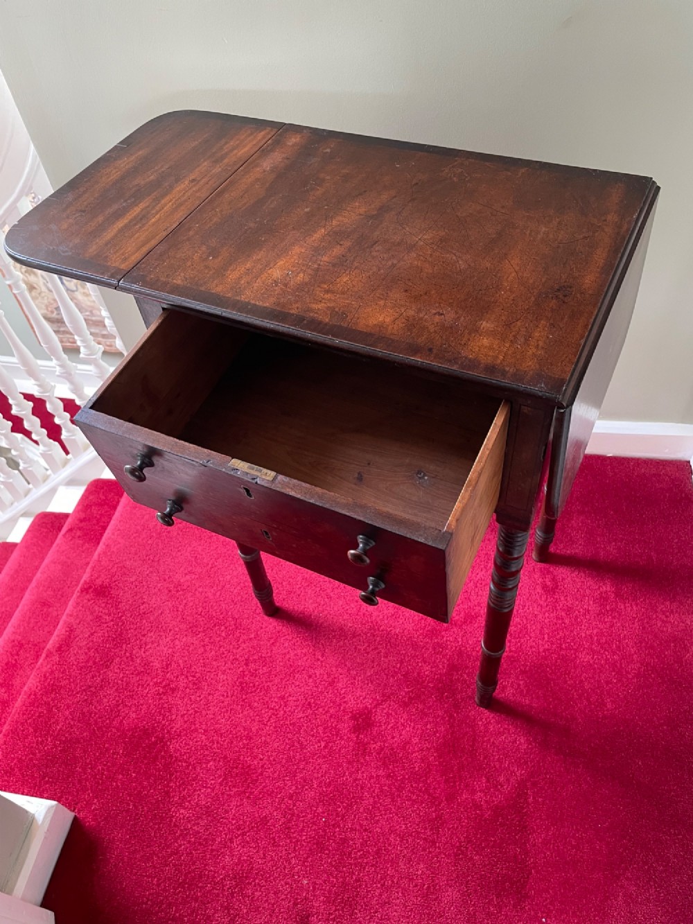 A dark mahogany drop-leaf side table featuring two drawers with wooden knobs and four slender turned legs. View III