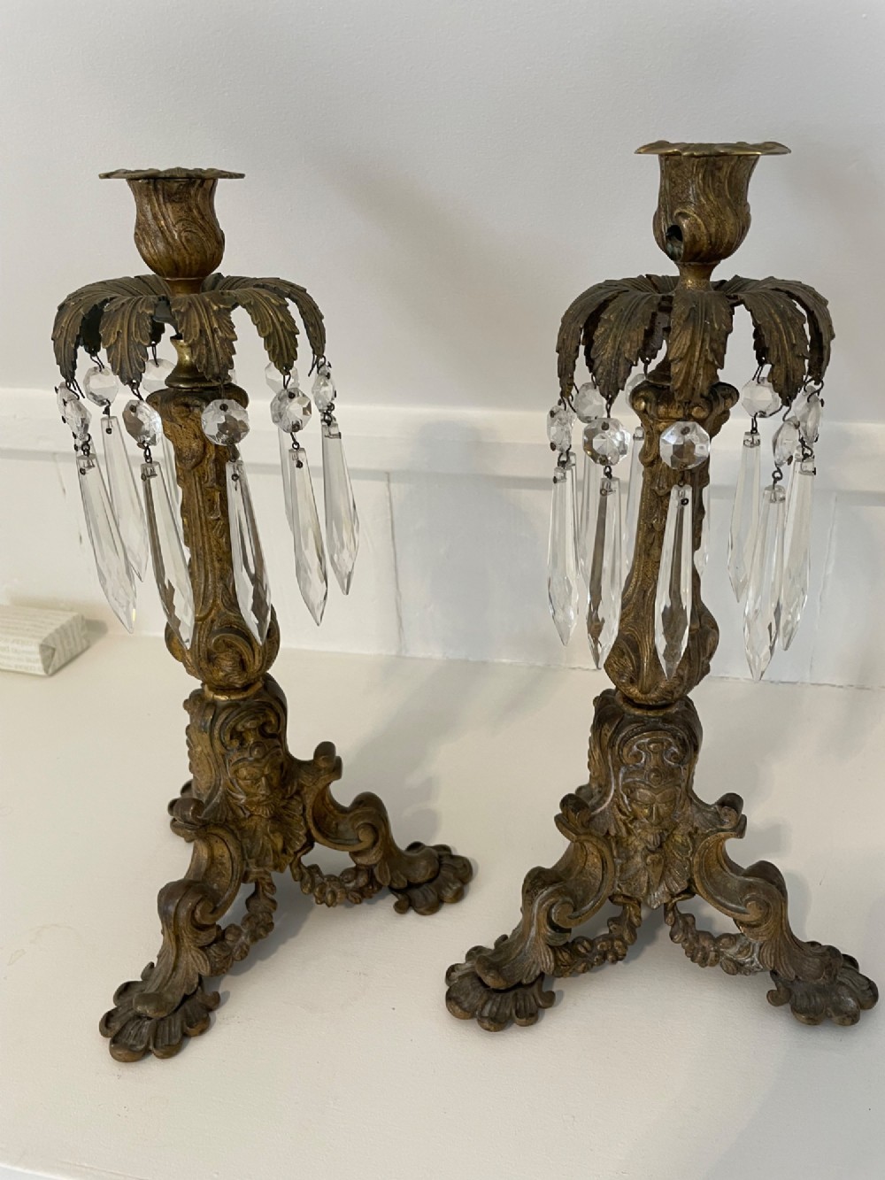 A pair of ornate gilt brass candlesticks featuring scrolling tripod bases, palm leaf collars, and hanging clear glass crystal drops. View II