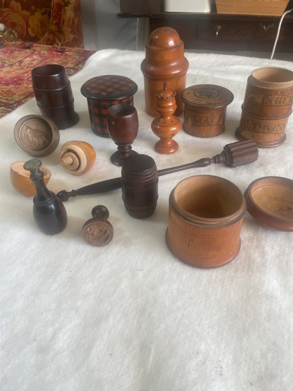 A collection of thirteen antique turned wooden treen objects including lidded spice pots, butter stamps, and small vessels arranged on a white surface.