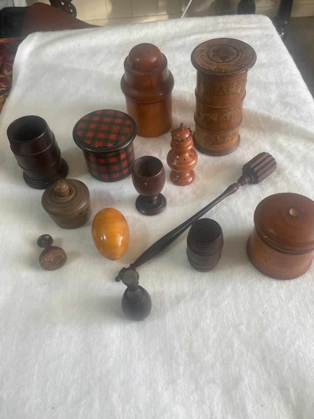A collection of thirteen antique turned wooden treen objects including lidded spice pots, butter stamps, and small vessels arranged on a white surface. View II