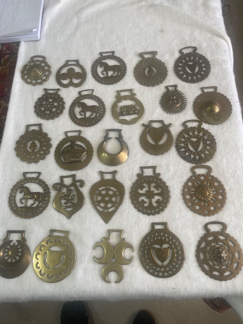 A collection of twenty-five assorted antique cast brass horse brasses displaying various pierced motif designs including horses, crowns, and geometric shapes.
