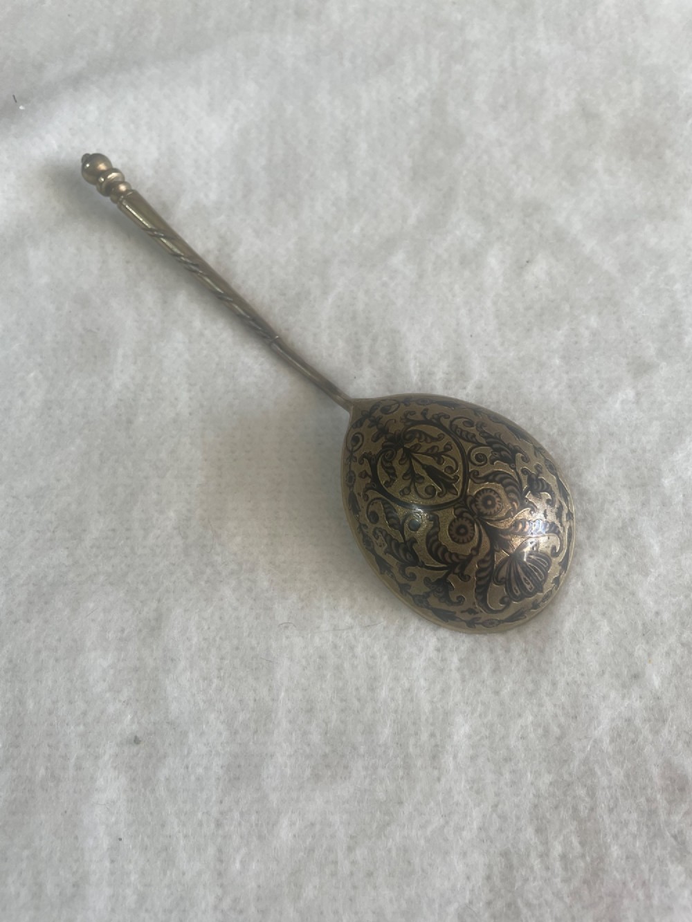 An antique Russian silver spoon featuring a twisted stem, a knopped finial, and an oval bowl decorated with black niello foliate scrollwork on the reverse.