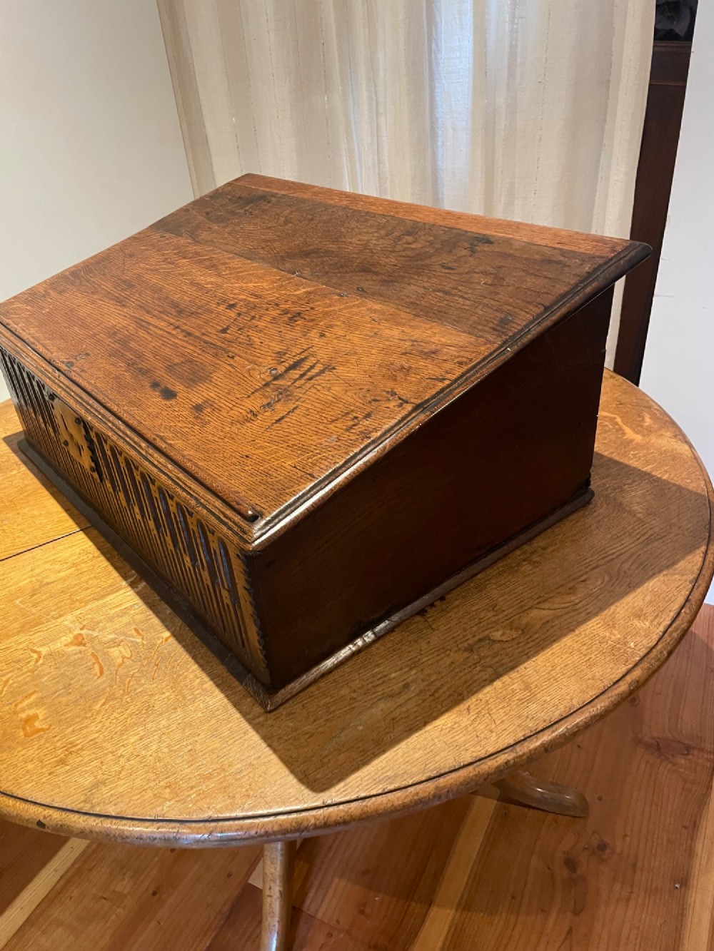 A rectangular warm brown oak bible box featuring a slanted hinged lid, carved vertical details on the front panel, and a central brass lock plate.