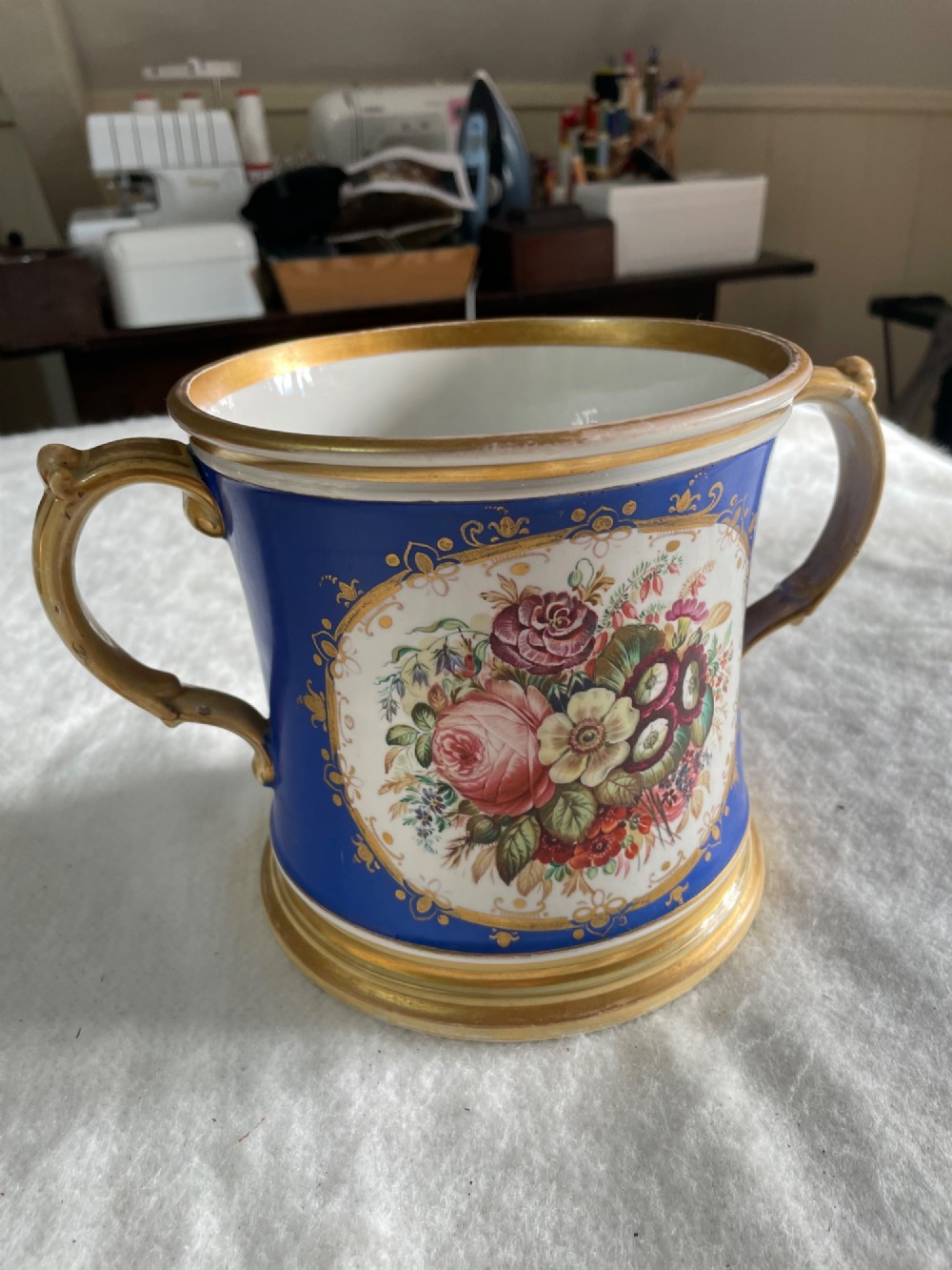 A cobalt blue porcelain two-handled loving cup featuring a hand-painted floral bouquet within a gilded ornate frame.