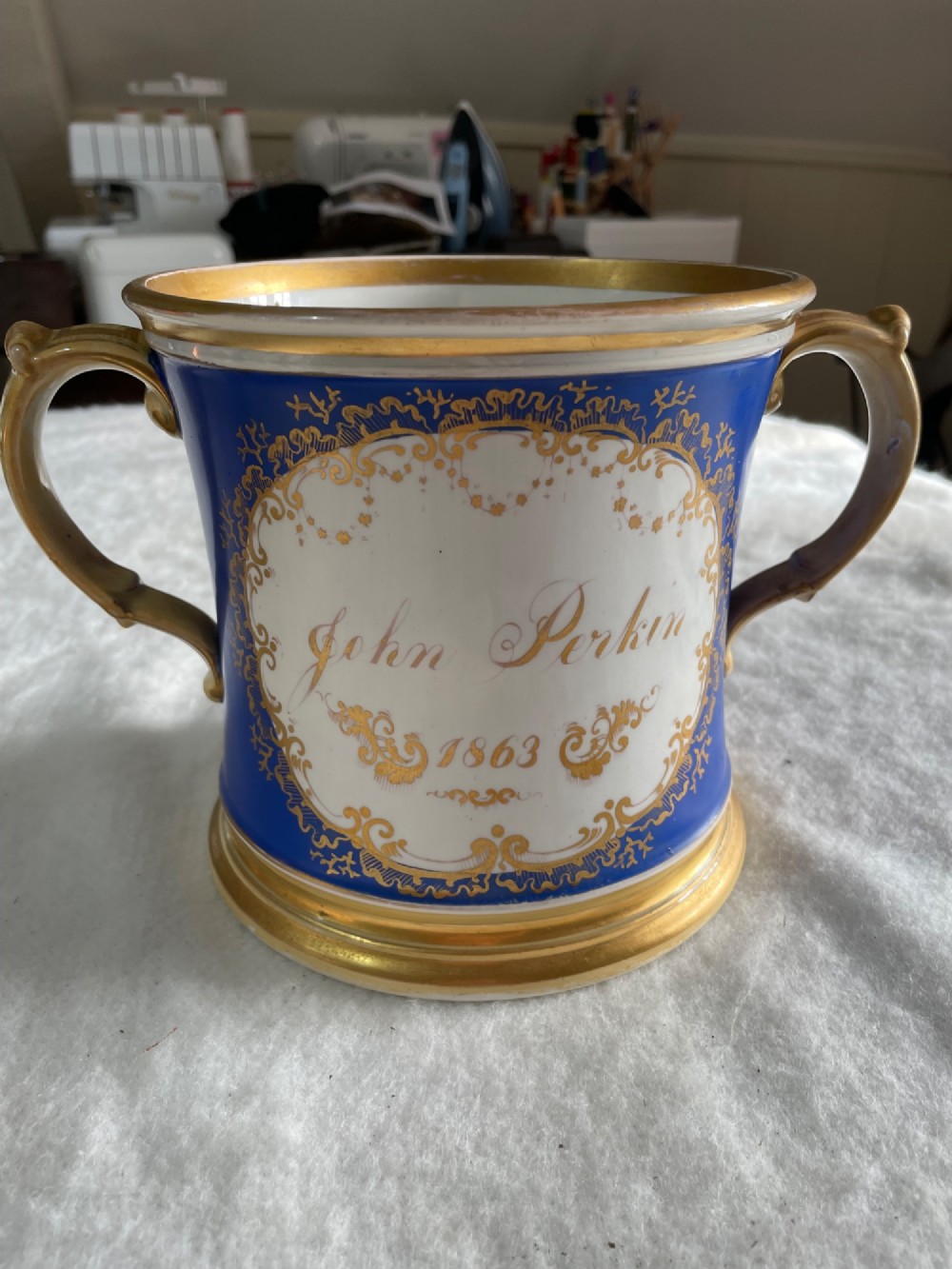 A cobalt blue porcelain two-handled loving cup featuring a hand-painted floral bouquet within a gilded ornate frame. View II