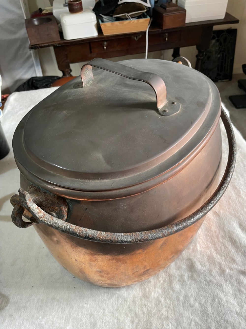 A large antique copper pot featuring a fitted lid with a copper handle and an arched iron swing handle.