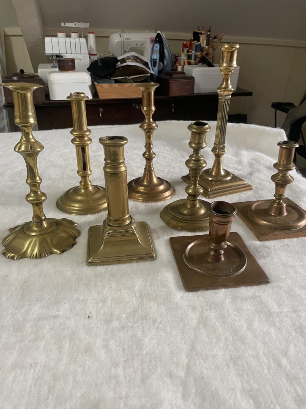 A group of eight early brass candlesticks displaying varied heights with square, round, and scalloped bases paired with turned and fluted stems. View II