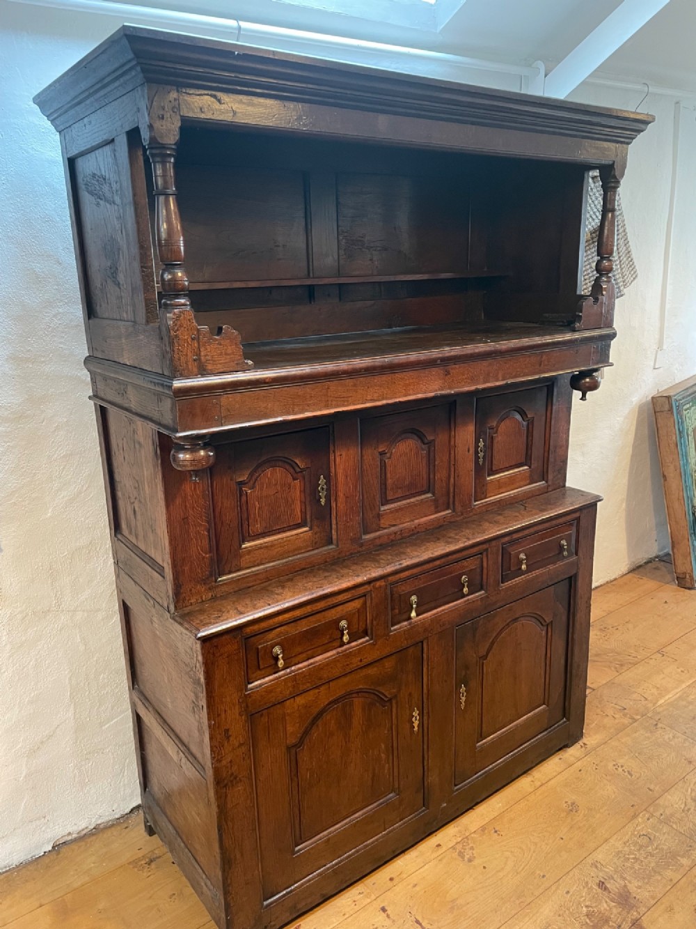 A dark oak three-tier Welsh tridarn featuring an open upper shelf with turned columns above a double-cupboard section and a lower base with drawers and doors. View II
