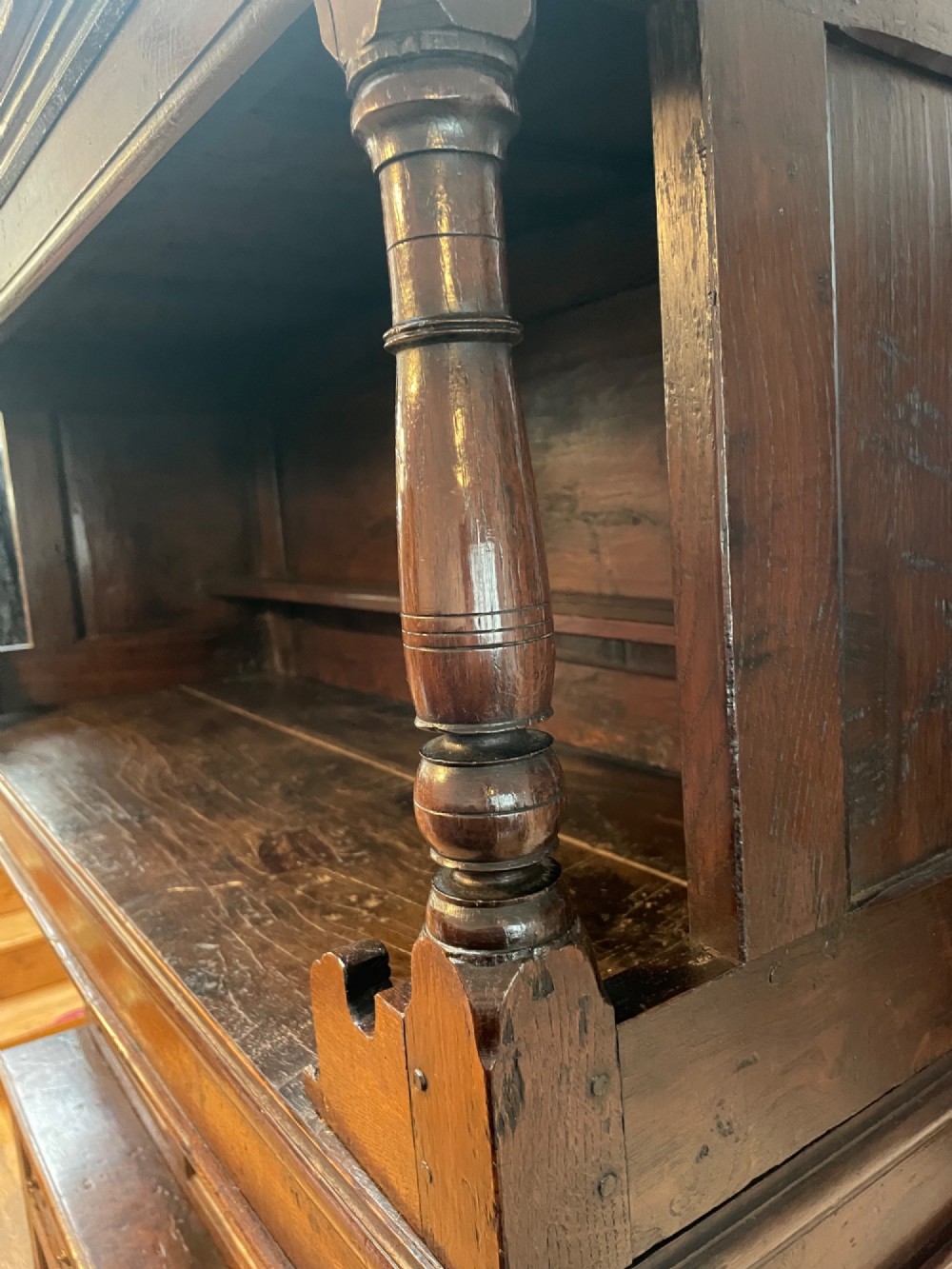 A dark oak three-tier Welsh tridarn featuring an open upper shelf with turned columns above a double-cupboard section and a lower base with drawers and doors. View III