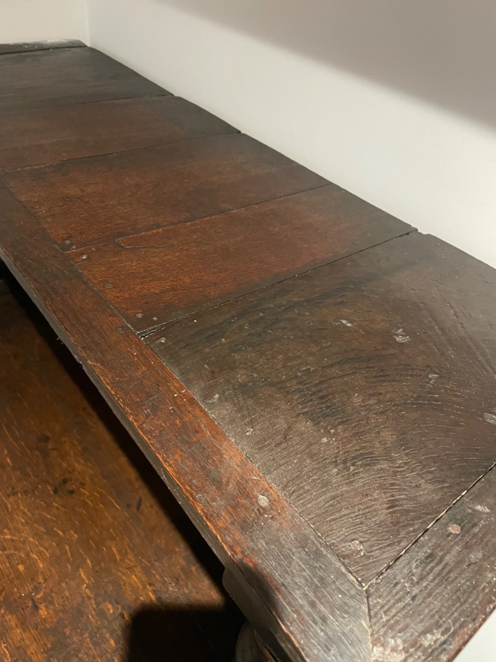 A dark carved oak court cupboard featuring an open upper shelf supported by turned balusters above two carved drawers and two panelled cupboard doors. View III