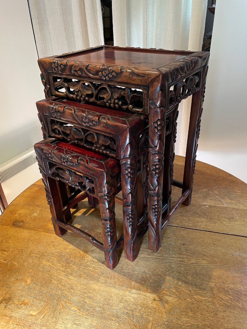 A set of three graduated dark hardwood Chinese nesting tables featuring carved grape friezes and bamboo-style legs.