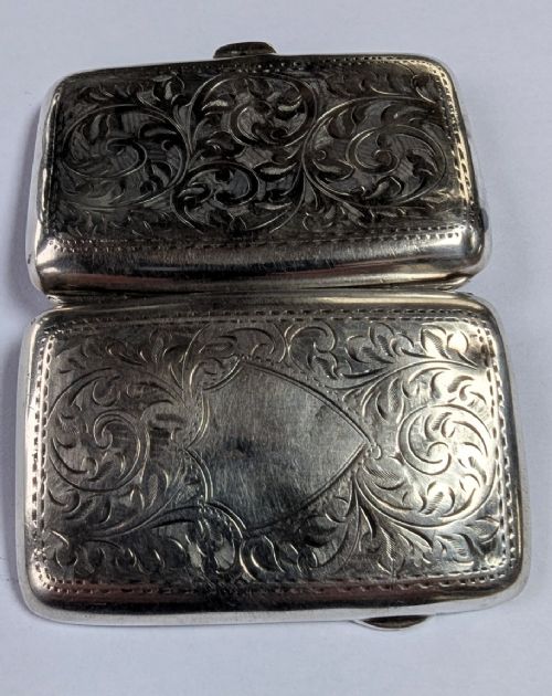 An open antique sterling silver cigarette case featuring hand-engraved foliate scrollwork and a blank shield cartouche on the outer cover. View IV