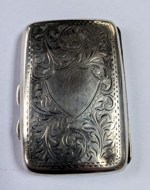 An open antique sterling silver cigarette case featuring hand-engraved foliate scrollwork and a blank shield cartouche on the outer cover. View V