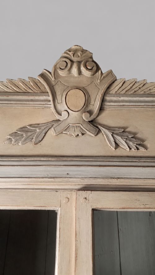 fig 1. A two-tier 19th-century French painted cupboard featuring upper glazed doors with a carved pediment and lower panelled cabinet doors.