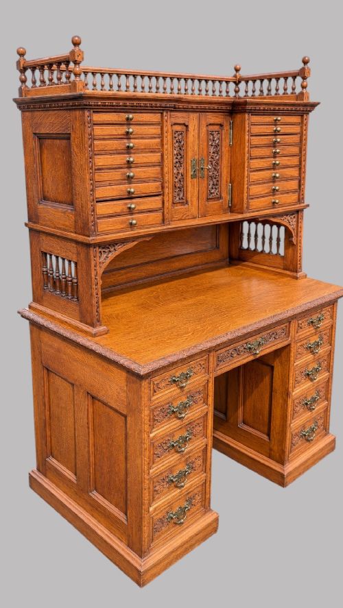 fig 1. A late Victorian quarter-sawn oak collectors desk featuring carved pedestals, multiple shallow drawer tiers, a central cupboard, and a top spindle gallery.