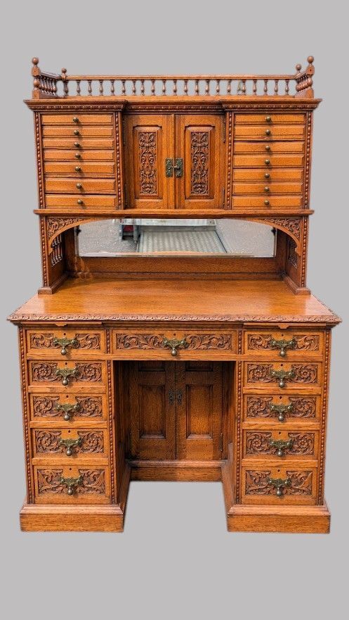 fig 2. A late Victorian carved oak kneehole desk featuring an upper gallery with drawers, spindles, carved doors, and a pedestal base.