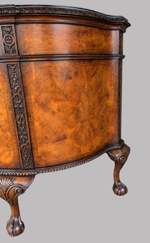 A bow-front burr walnut sideboard with carved pilasters, twin cupboard doors, a top drawer, and four carved cabriole legs ending in ball and claw feet. View V