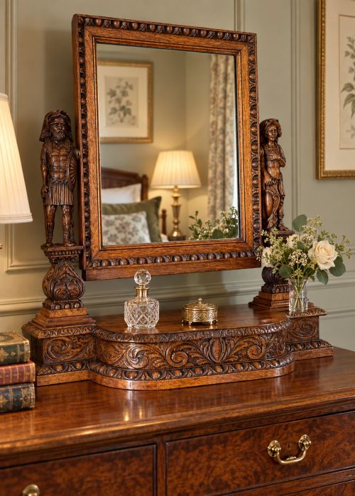fig 1. A carved oak dressing mirror featuring a rectangular frame flanked by two carved human figures resting on an ornate plinth base.