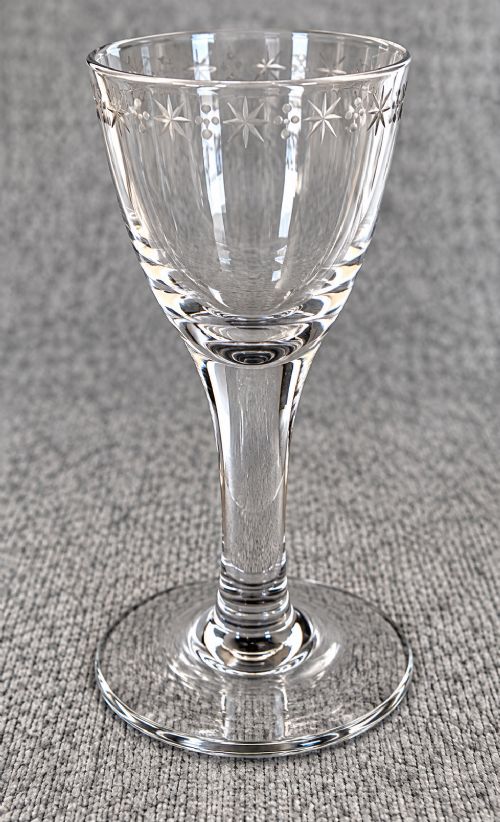 An antique clear lead glass dram glass featuring a flared rim with wheel-engraved starburst motifs, a solid thick stem, and a flat circular foot. View III