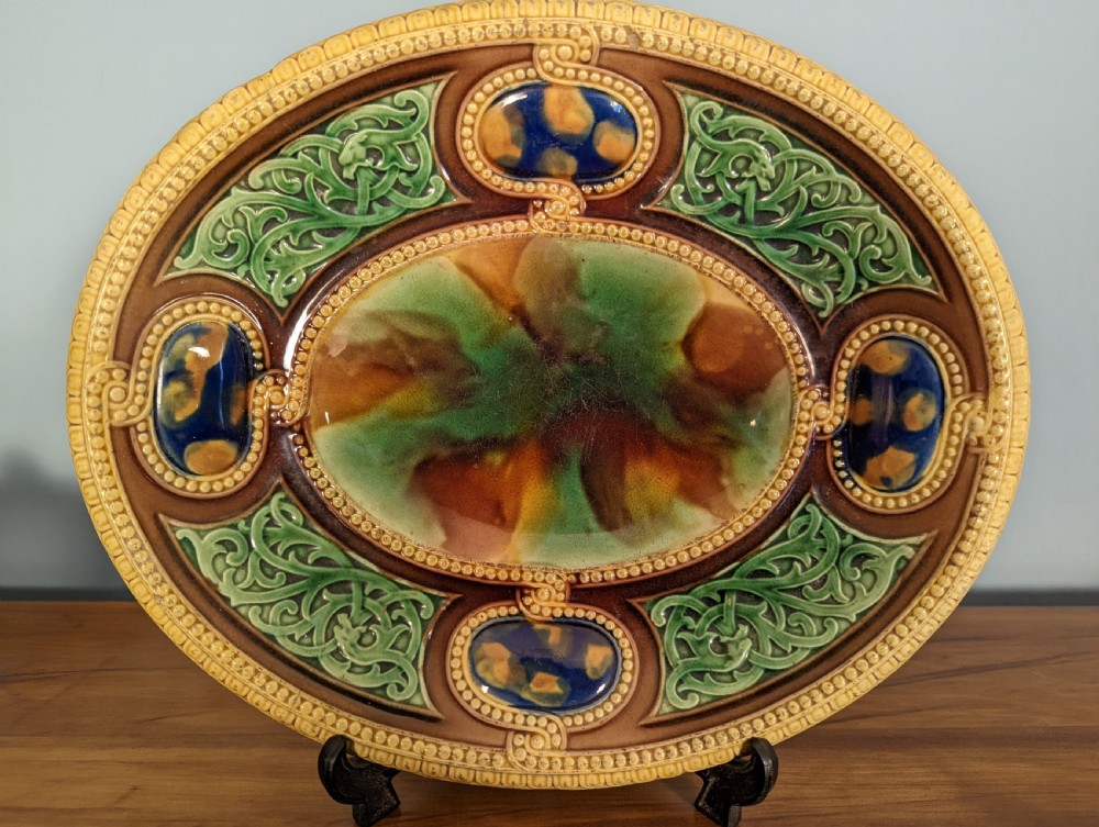 An oval Victorian majolica decorative ceramic dish featuring relief foliage, cobalt cabochons, and mottled green and brown lead glazing.