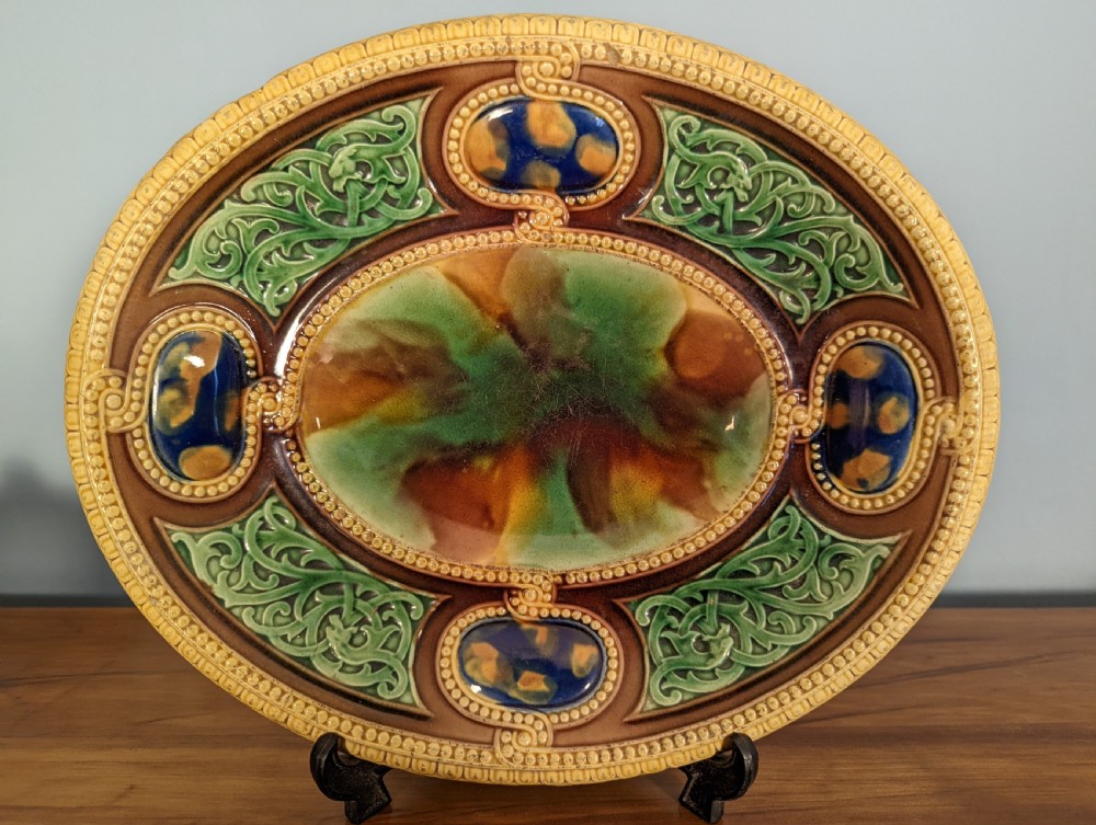 An oval Victorian majolica decorative ceramic dish featuring relief foliage, cobalt cabochons, and mottled green and brown lead glazing. View II
