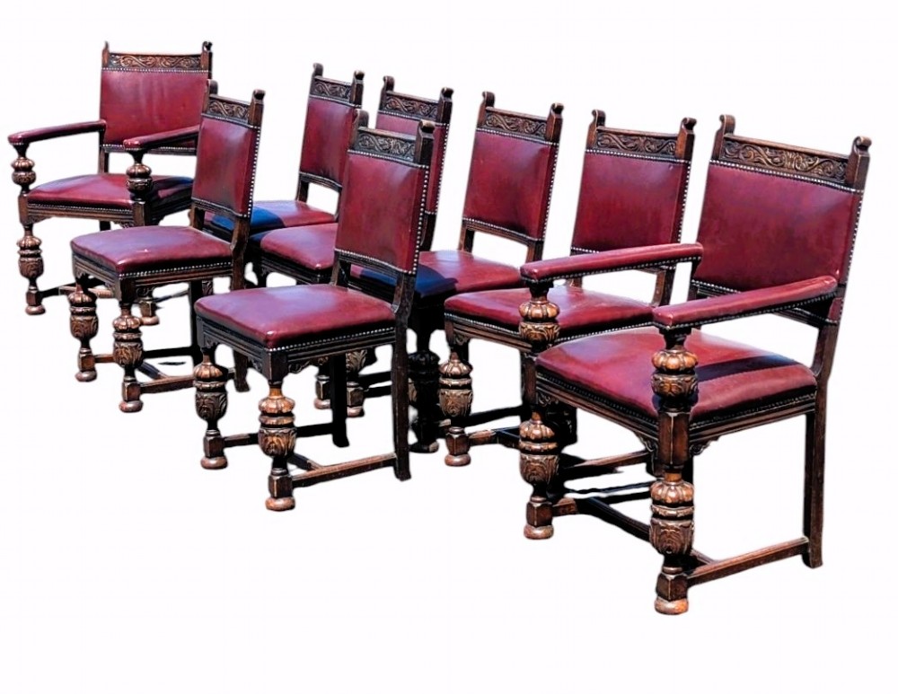 Set of eight dark oak dining chairs with carved top rails, turned legs, and burgundy leather upholstery secured with brass studs.