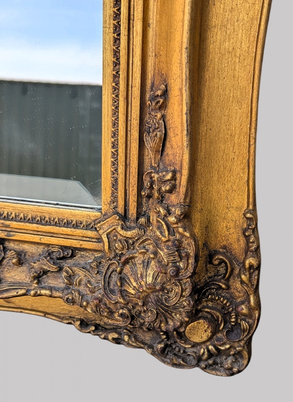 An elongated vertical giltwood pier mirror featuring an upper painted landscape panel above a rectangular glass mirror, set within a carved rococo-style frame. View V