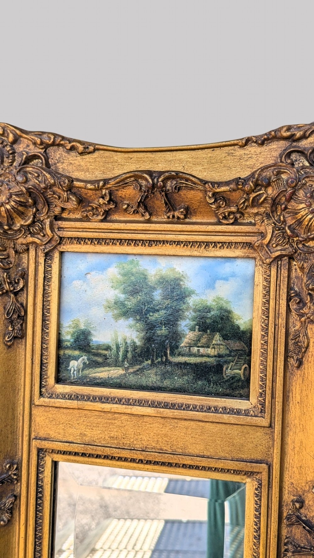 An elongated vertical giltwood pier mirror featuring an upper painted landscape panel above a rectangular glass mirror, set within a carved rococo-style frame. View VII