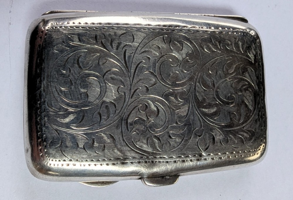 An open antique sterling silver cigarette case featuring hand-engraved foliate scrollwork and a blank shield cartouche on the outer cover. View VI