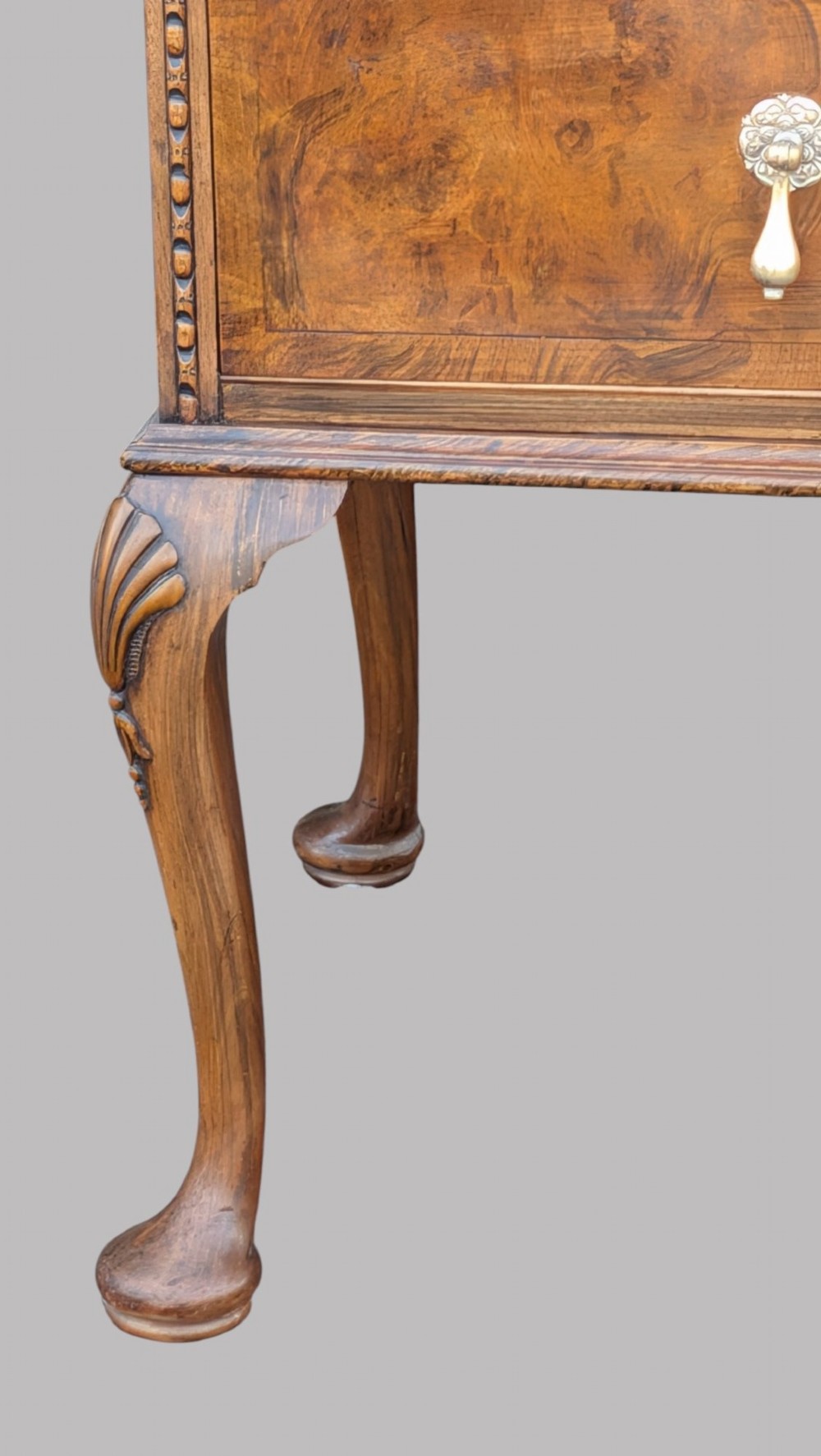 A Queen Anne style burr walnut chest of drawers featuring two short over two long drawers, brass drop handles, and carved cabriole legs. View V