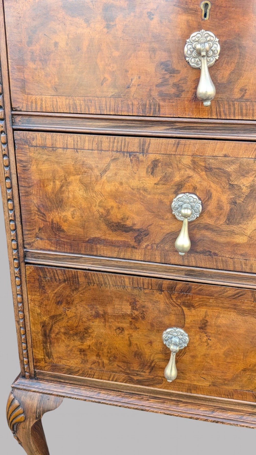 A Queen Anne style burr walnut chest of drawers featuring two short over two long drawers, brass drop handles, and carved cabriole legs. View XII