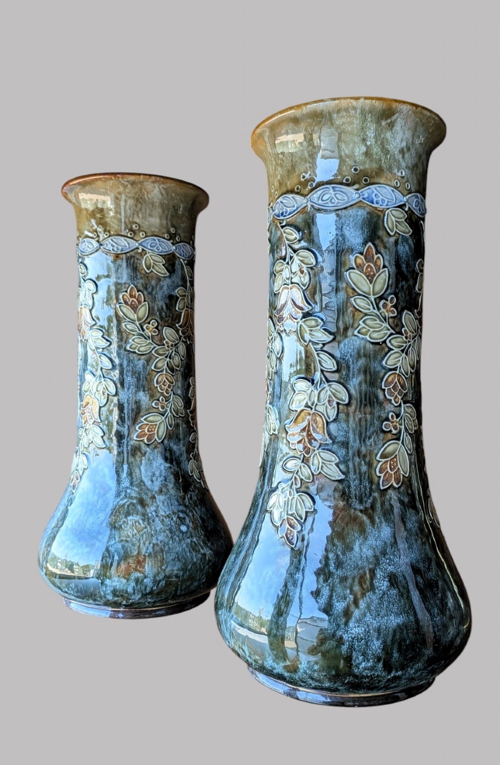 A matching pair of Art Nouveau stoneware vases featuring flared bases, mottled blue and brown glazes, and stylised floral relief decoration.