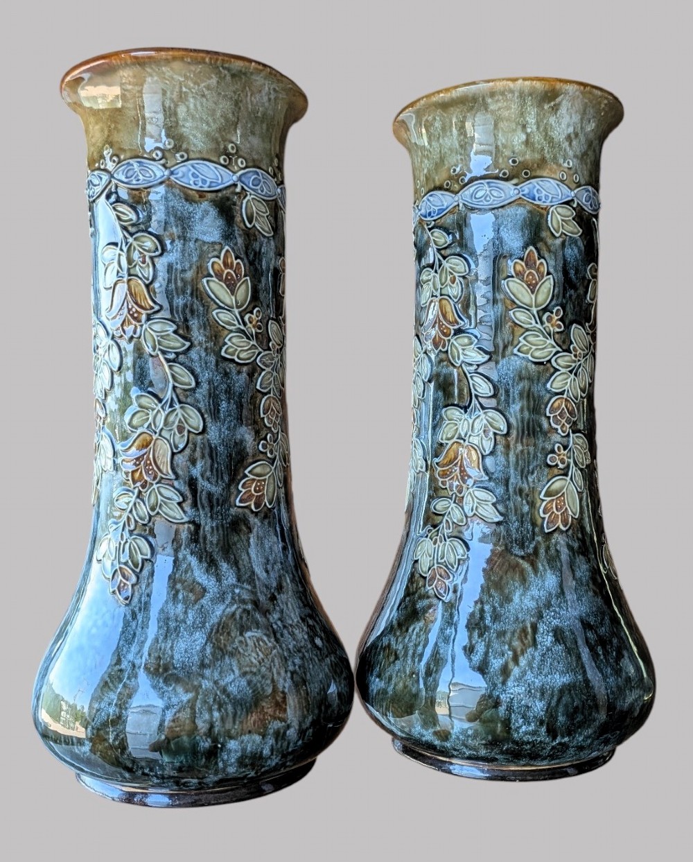 A matching pair of Art Nouveau stoneware vases featuring flared bases, mottled blue and brown glazes, and stylised floral relief decoration. View II