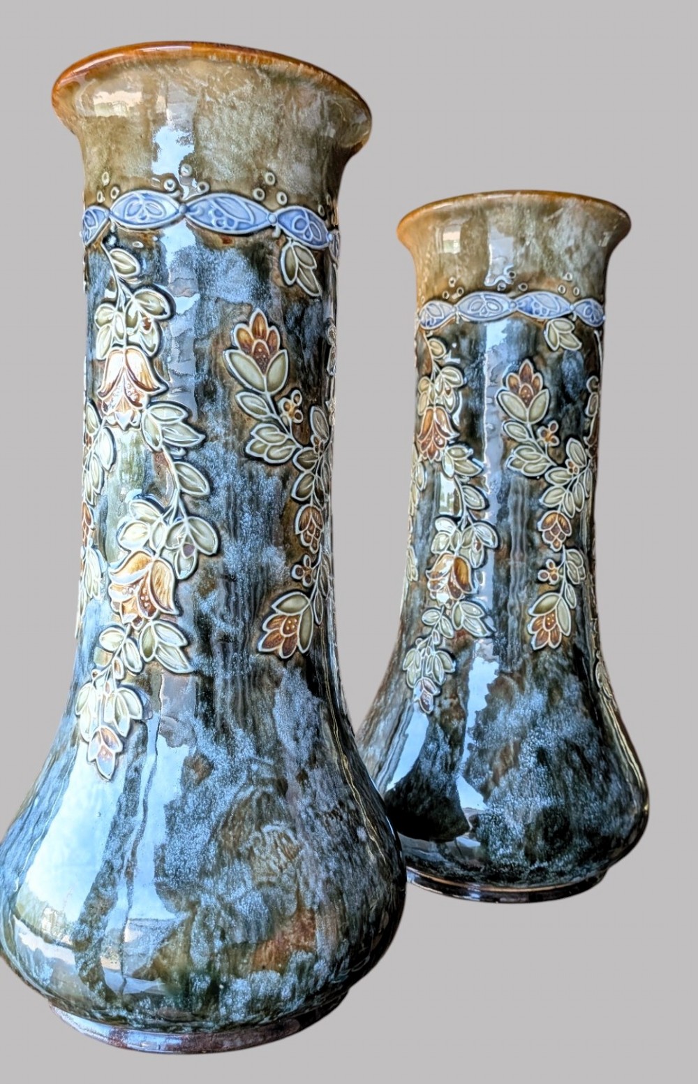 A matching pair of Art Nouveau stoneware vases featuring flared bases, mottled blue and brown glazes, and stylised floral relief decoration. View IV