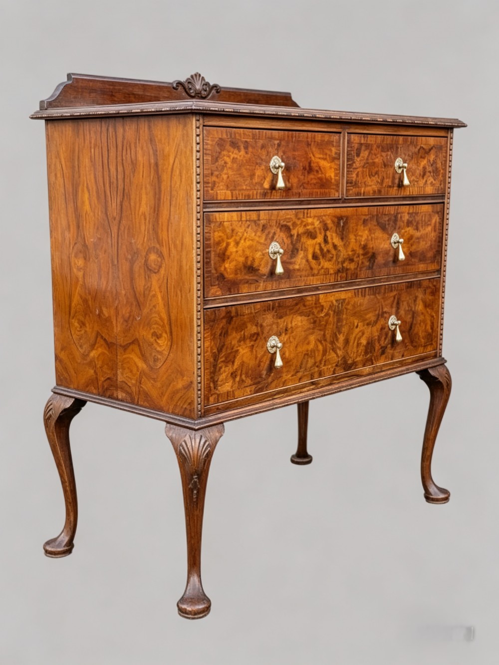 A Queen Anne style burr walnut chest of drawers featuring two short over two long drawers, brass drop handles, and carved cabriole legs. View XIV