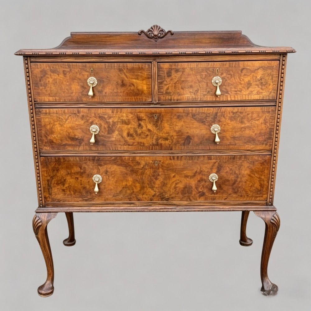 A Queen Anne style burr walnut chest of drawers featuring two short over two long drawers, brass drop handles, and carved cabriole legs.