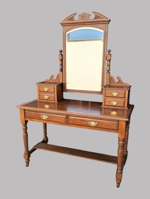An Edwardian walnut dressing table with an upright swivelling mirror, carved pediment cresting, four drawers, turned legs, and brass hardware.