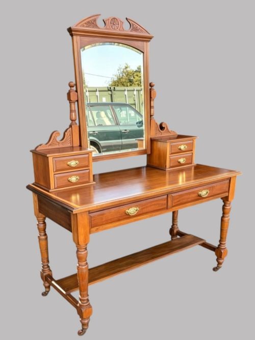 An Edwardian walnut dressing table with an upright swivelling mirror, carved pediment cresting, four drawers, turned legs, and brass hardware. View II