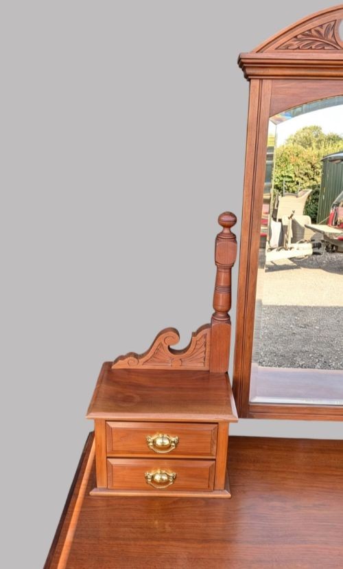 An Edwardian walnut dressing table with an upright swivelling mirror, carved pediment cresting, four drawers, turned legs, and brass hardware. View V