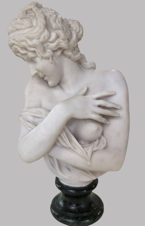 A carved white marble bust of a young woman with coiled hair and draped classical attire, mounted on a dark green marble circular plinth. View VI