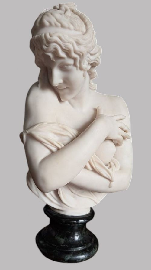 A carved white marble bust of a young woman with coiled hair and draped classical attire, mounted on a dark green marble circular plinth. View VII