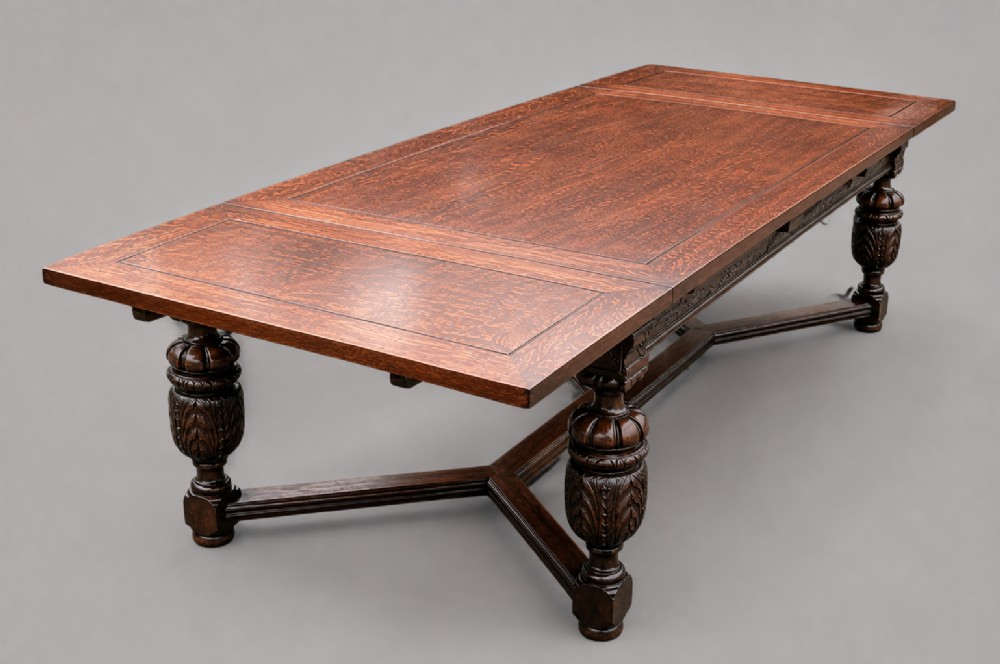 A rectangular extending oak dining table showing a quarter-sawn timber surface and carved bulbous legs underneath.