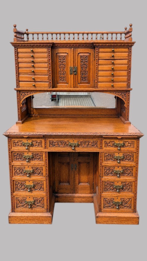 A late Victorian quarter-sawn oak collectors desk featuring carved pedestals, multiple shallow drawer tiers, a central cupboard, and a top spindle gallery. View IV
