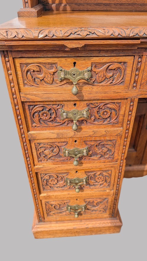 A late Victorian quarter-sawn oak collectors desk featuring carved pedestals, multiple shallow drawer tiers, a central cupboard, and a top spindle gallery. View IX