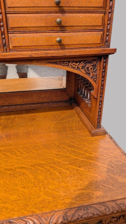 A late Victorian quarter-sawn oak collectors desk featuring carved pedestals, multiple shallow drawer tiers, a central cupboard, and a top spindle gallery. View X